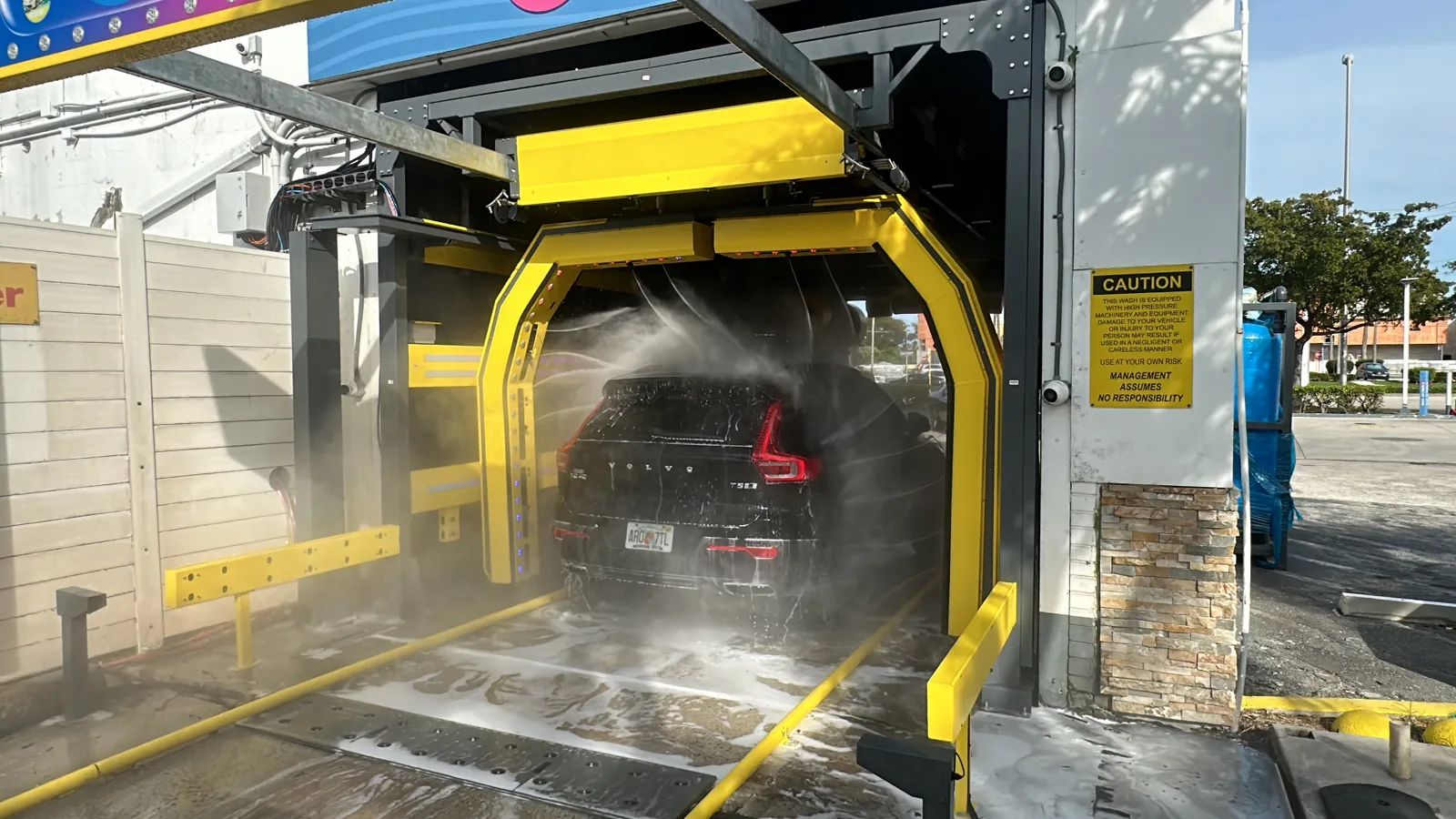 Water spraying from two rollover arms over a black SUV in an open-sided wash bay