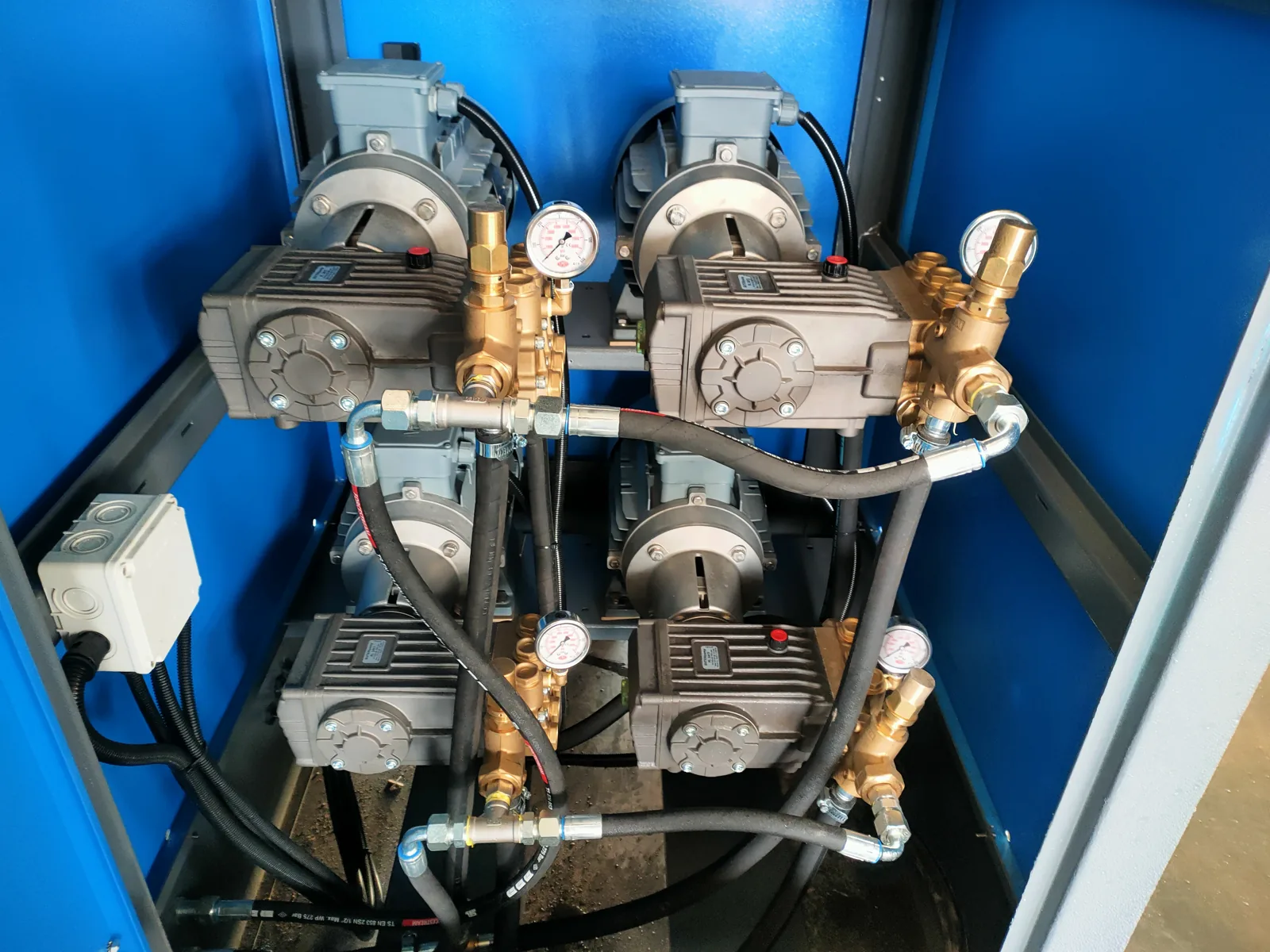 Four high-pressure pump heads with pressure gauges and braided hoses mounted in a blue cabin